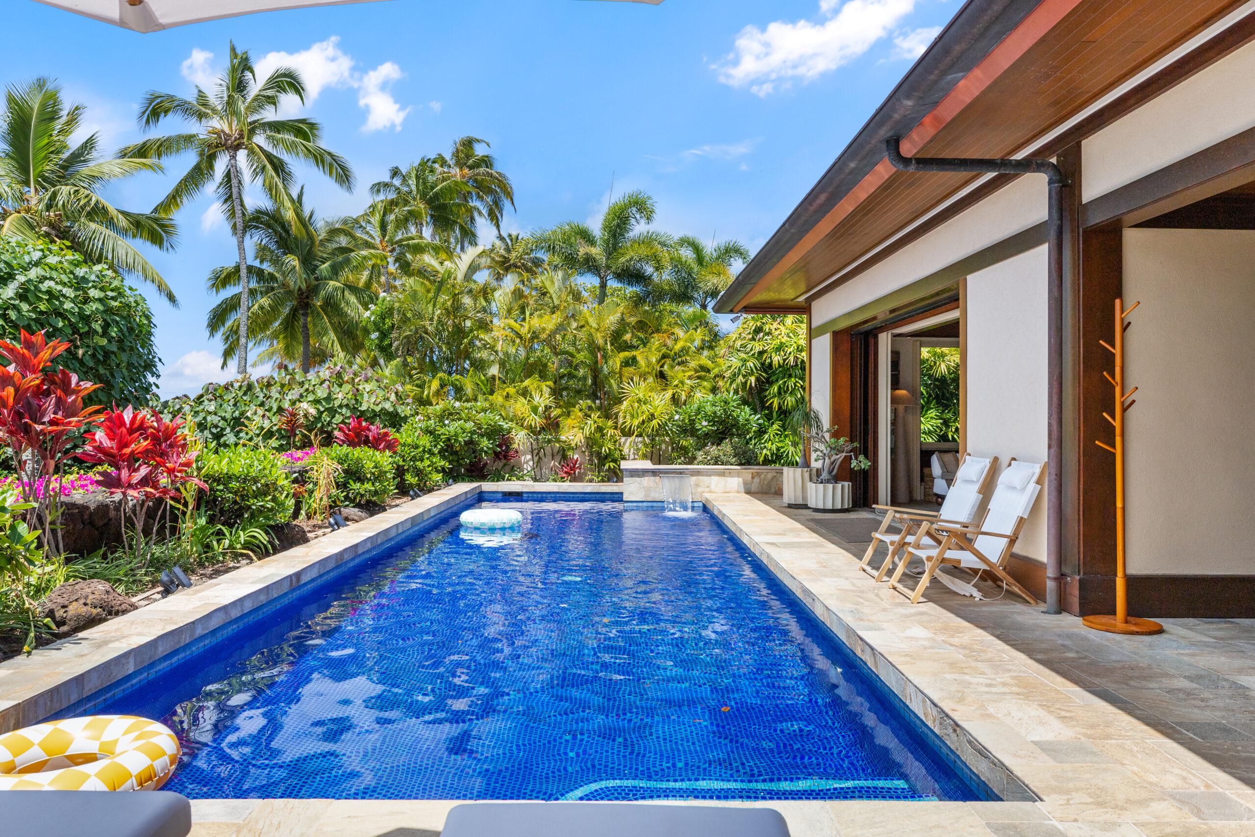 Private pool with loungers, lush tropical landscaping, and open-air living and dining room visible in the background