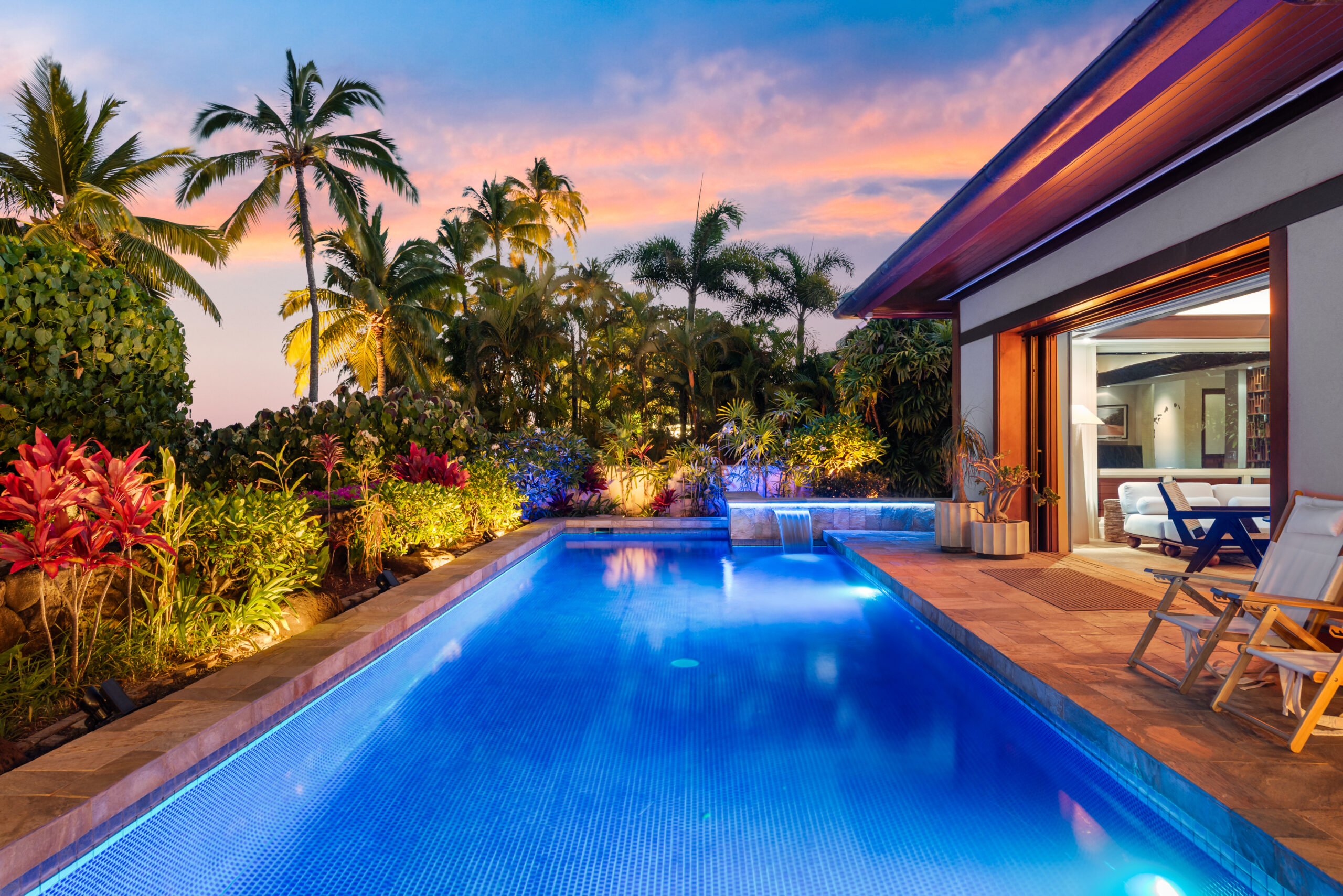 Private pool with loungers, lush tropical landscaping, and open-air living and dining room visible in the background