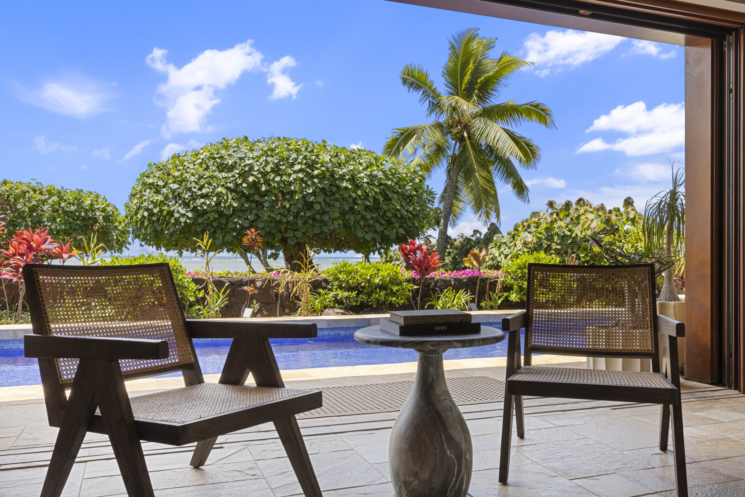 Two side chairs in open-air living room facing private pool and ocean, framed by tropical landscape and coastal light