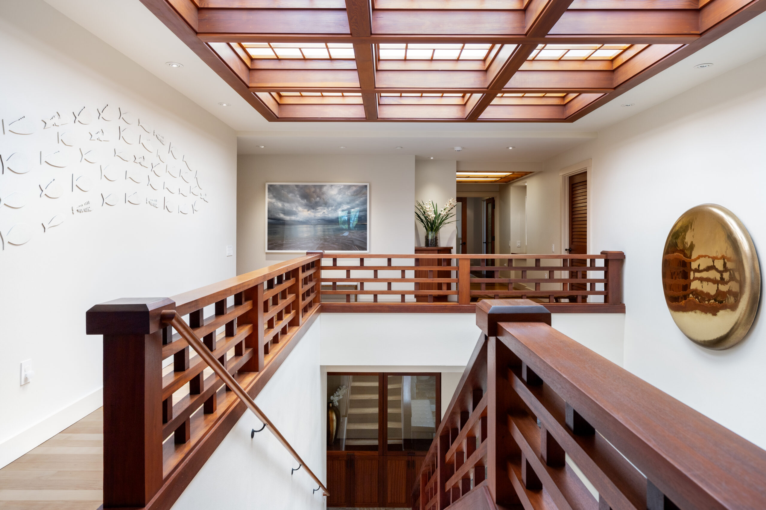 Elegant upper level hallway featuring dramatic coffered wood ceiling with integrated skylight, geometric wood railings, hardwood floors, textured accent wall, and views to lower level with natural lighting.