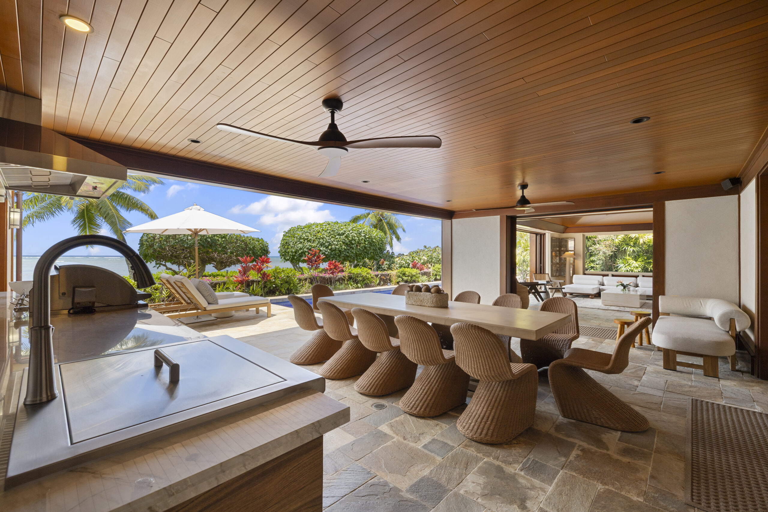 Outdoor dining area with seating for 12, open-air gourmet kitchen, and tropical surroundings
