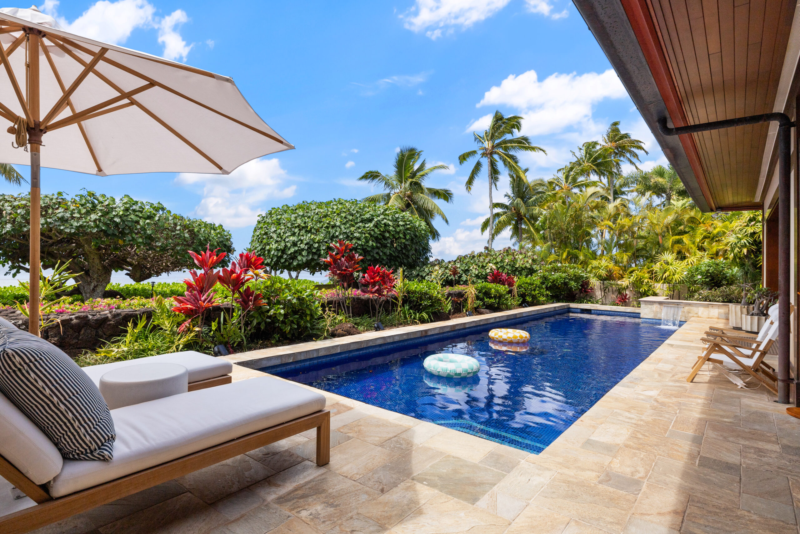 Private pool with loungers, lush tropical landscaping, and open-air living and dining room visible in the background