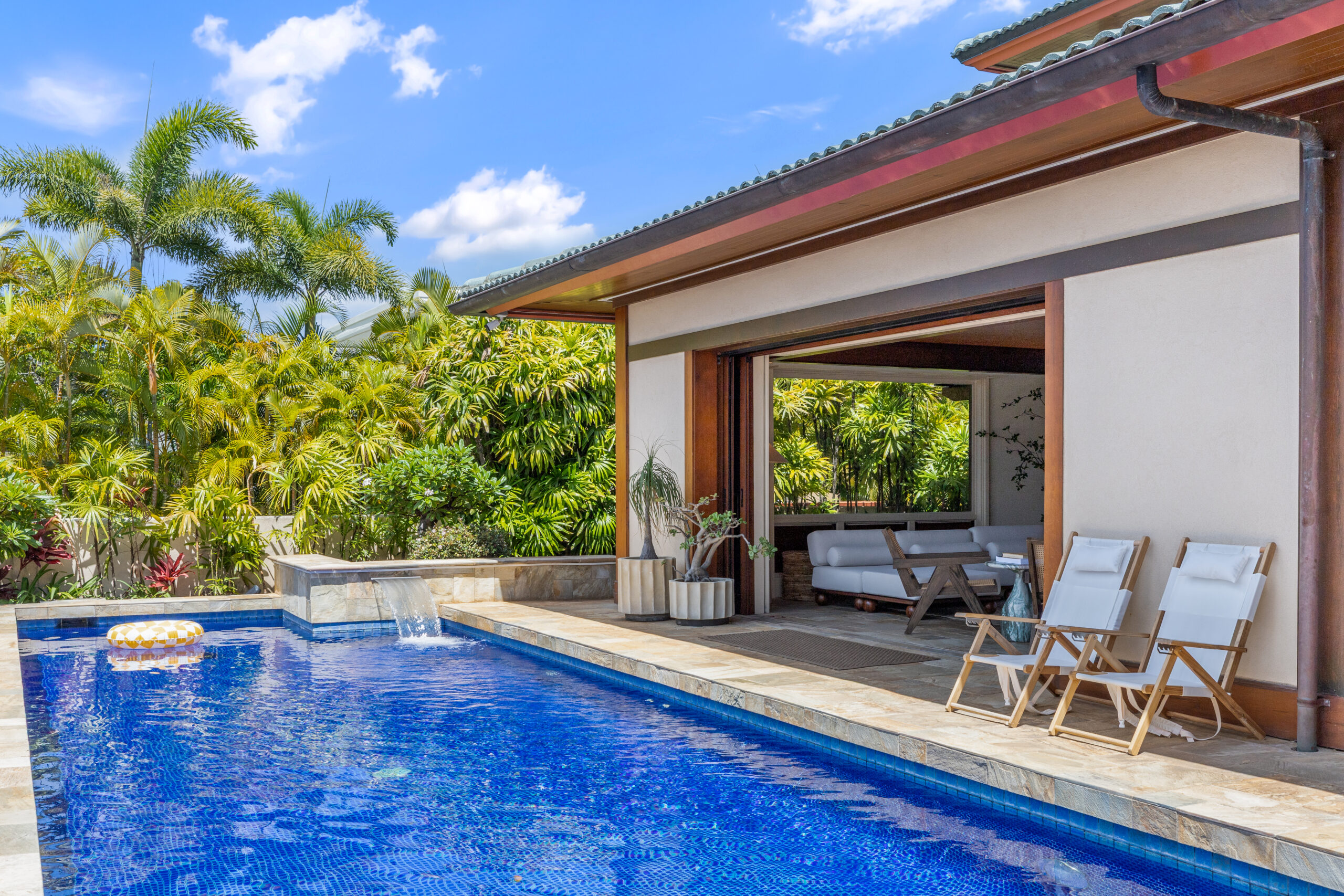 Private pool with loungers, lush tropical landscaping, and open-air living and dining room visible in the background
