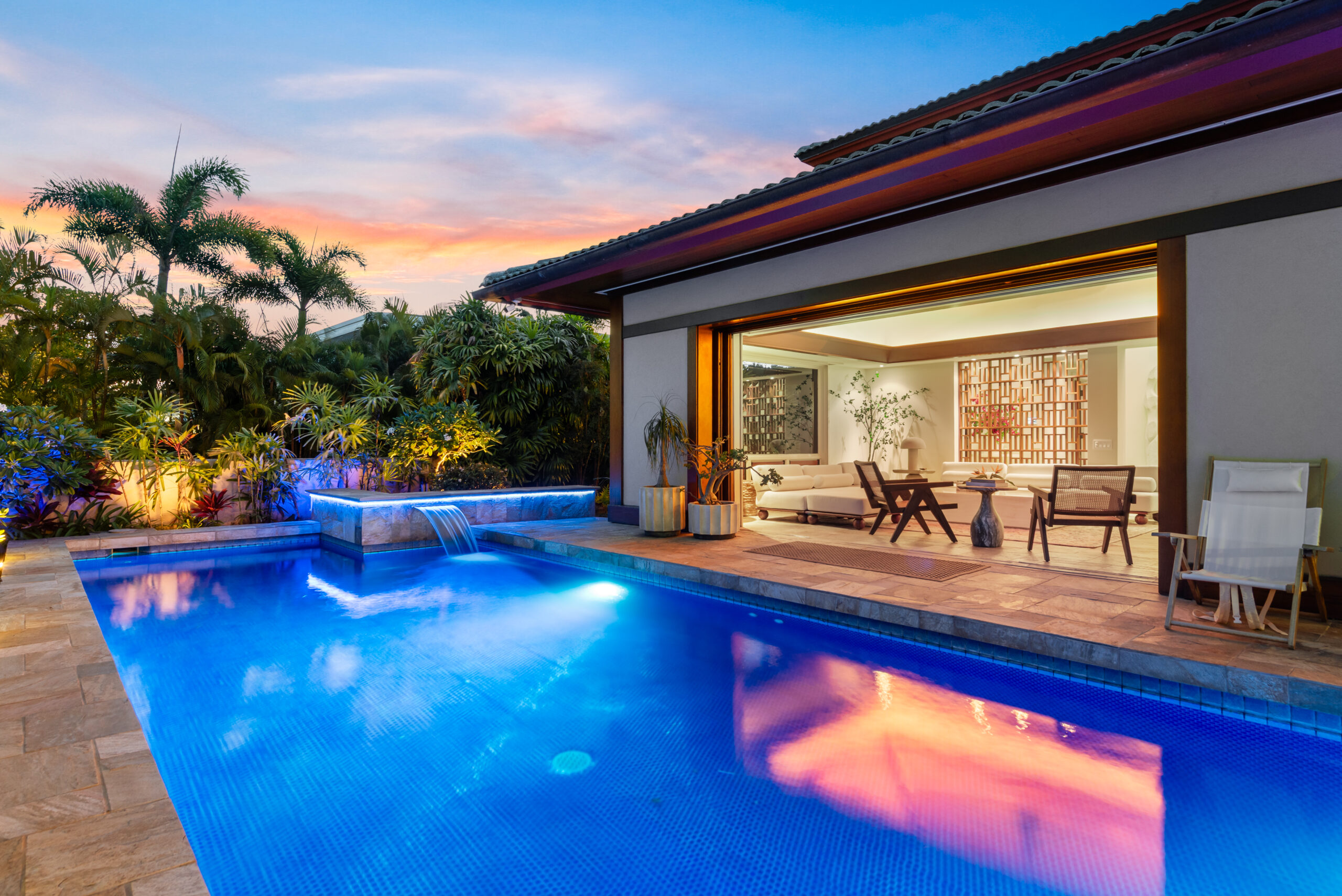Private pool with loungers, lush tropical landscaping, and open-air living and dining room visible in the background