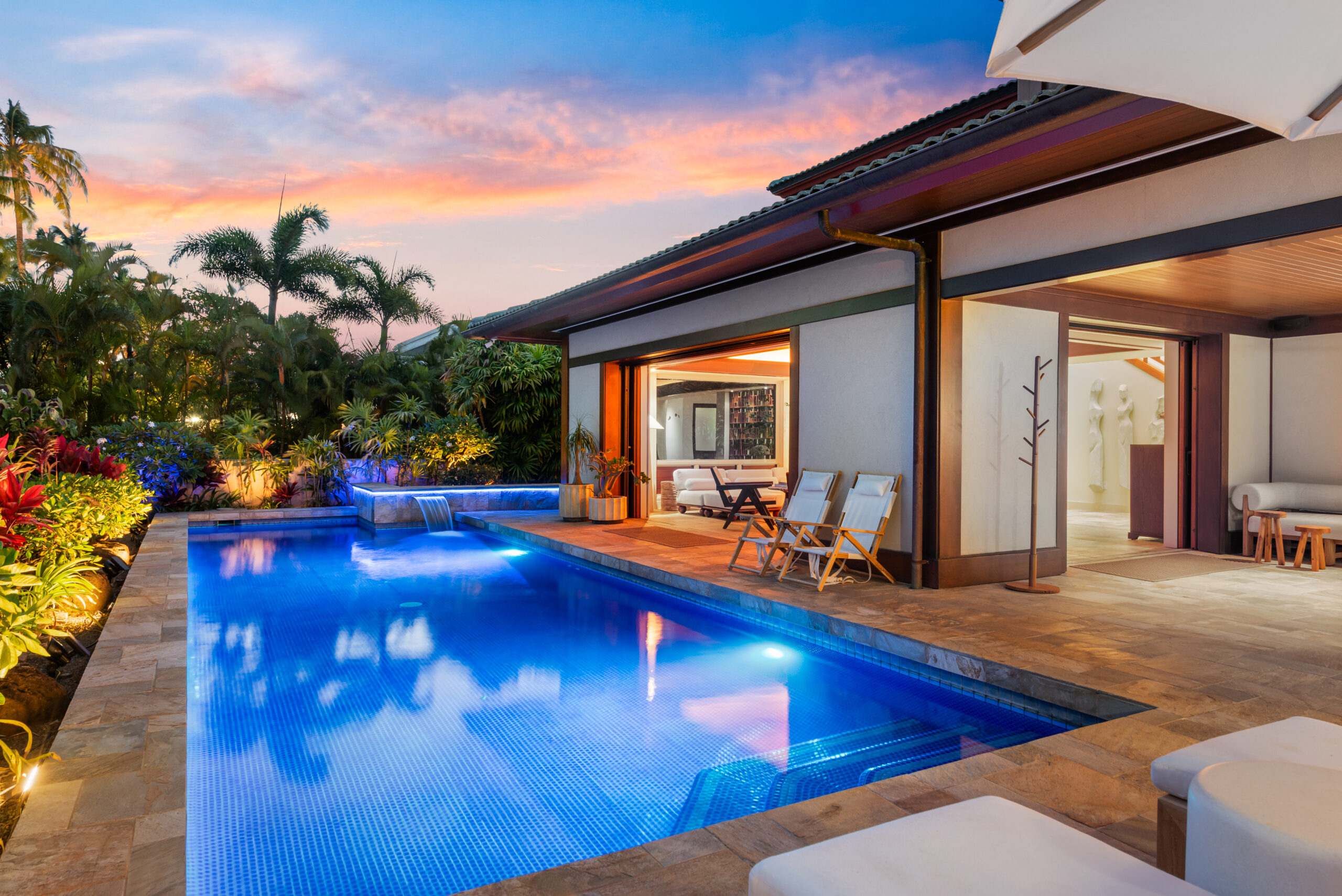 Private pool with loungers, lush tropical landscaping, and open-air living and dining room visible in the background