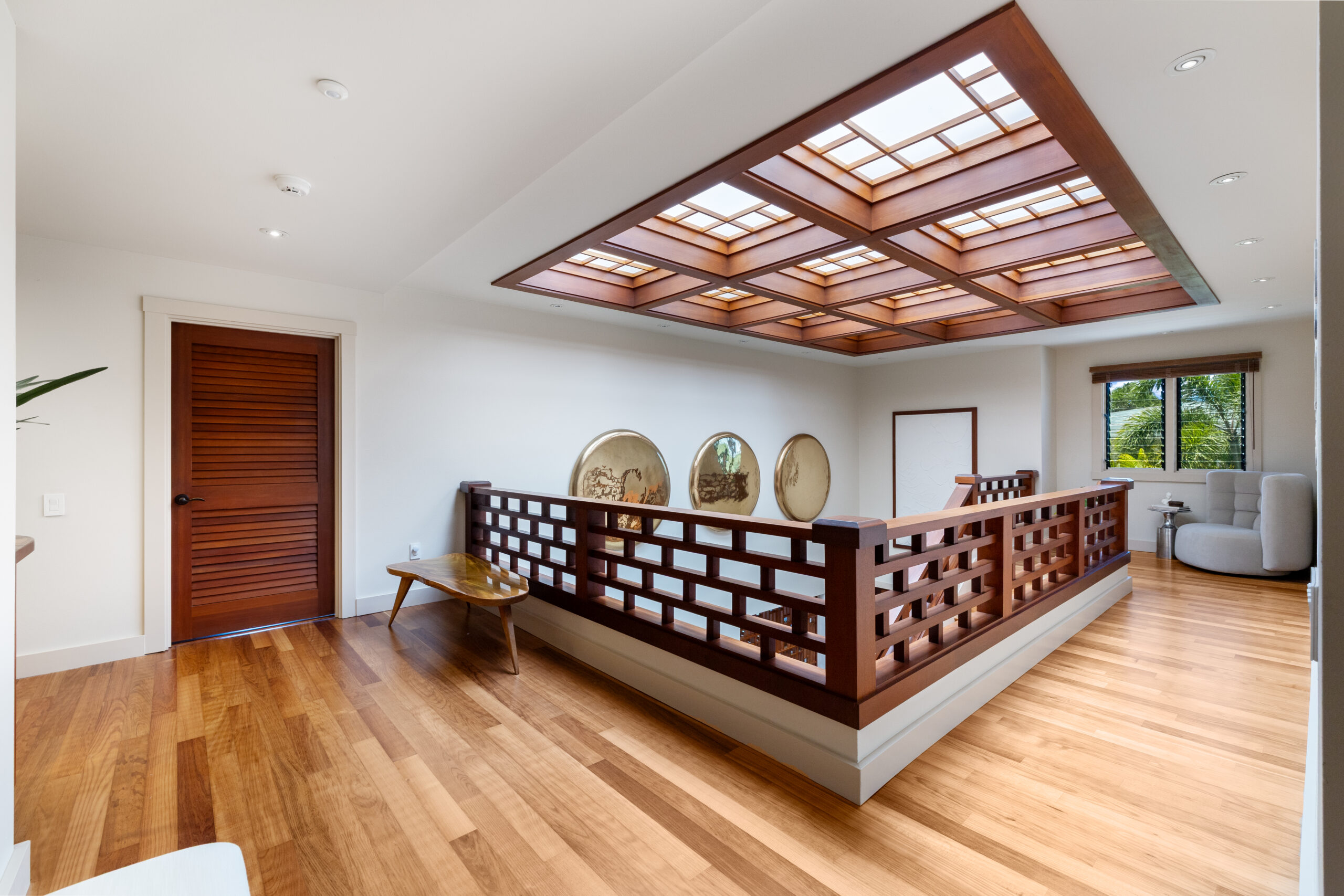 Elegant upper level hallway featuring dramatic coffered wood ceiling with integrated skylight, geometric wood railings, hardwood floors, textured accent wall, and views to lower level with natural lighting.