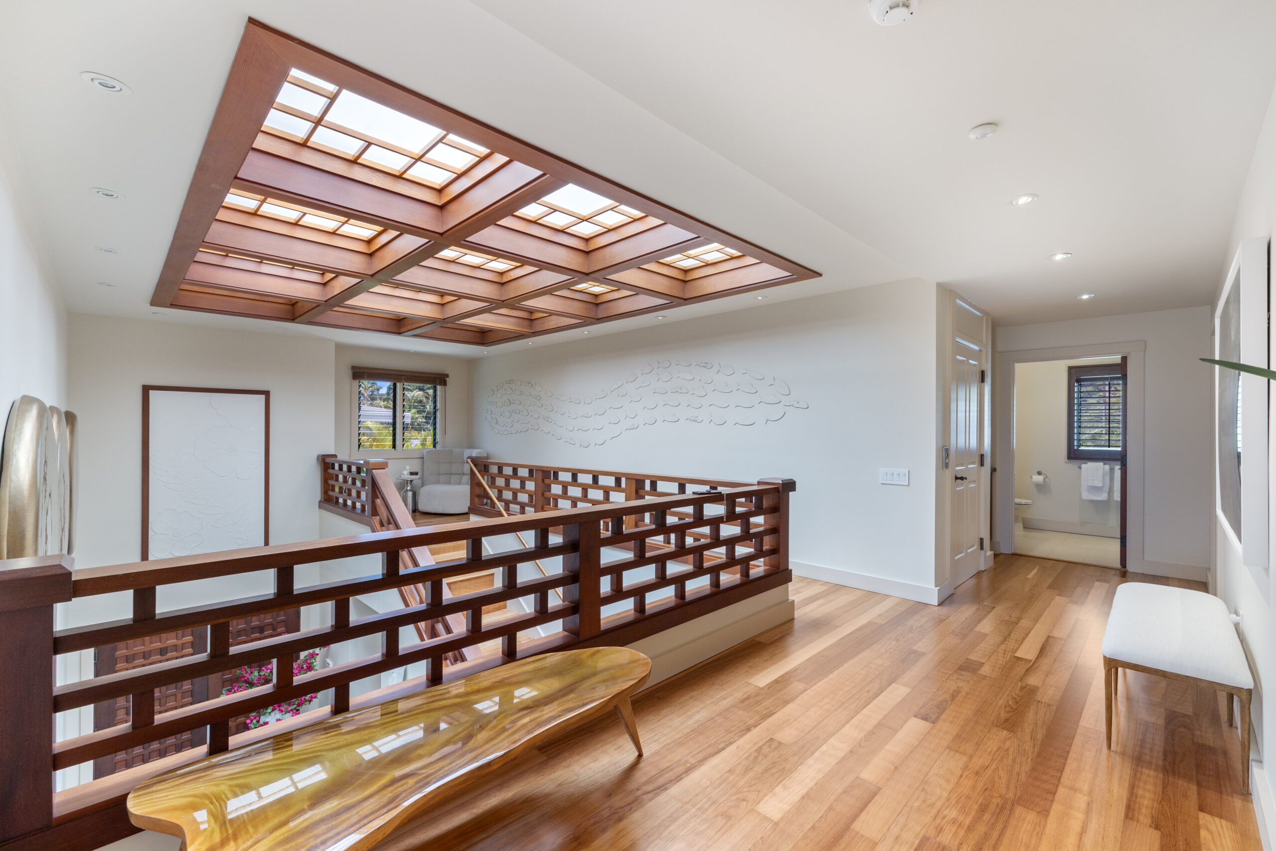 Elegant upper level hallway featuring dramatic coffered wood ceiling with integrated skylight, geometric wood railings, hardwood floors, textured accent wall, and views to lower level with natural lighting.