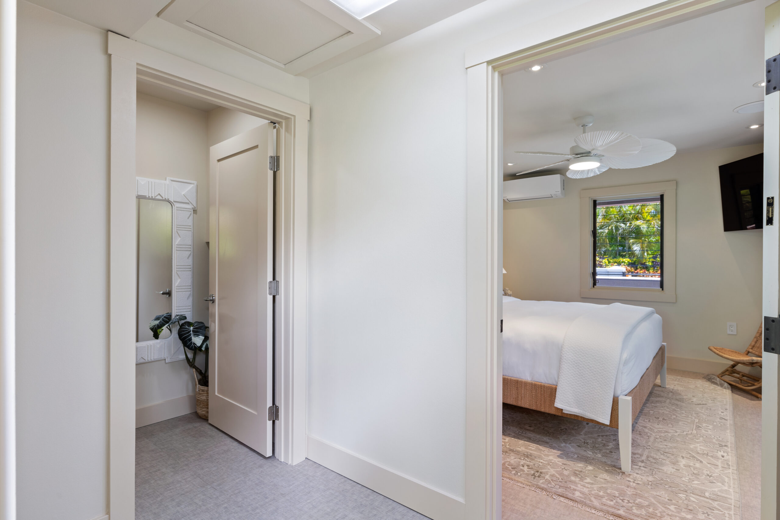 Serene guest bedroom with king bed, white linens, ceiling fan, and view into private en-suite bathroom with modern fixtures and white tile, featuring clean contemporary design and garden access.