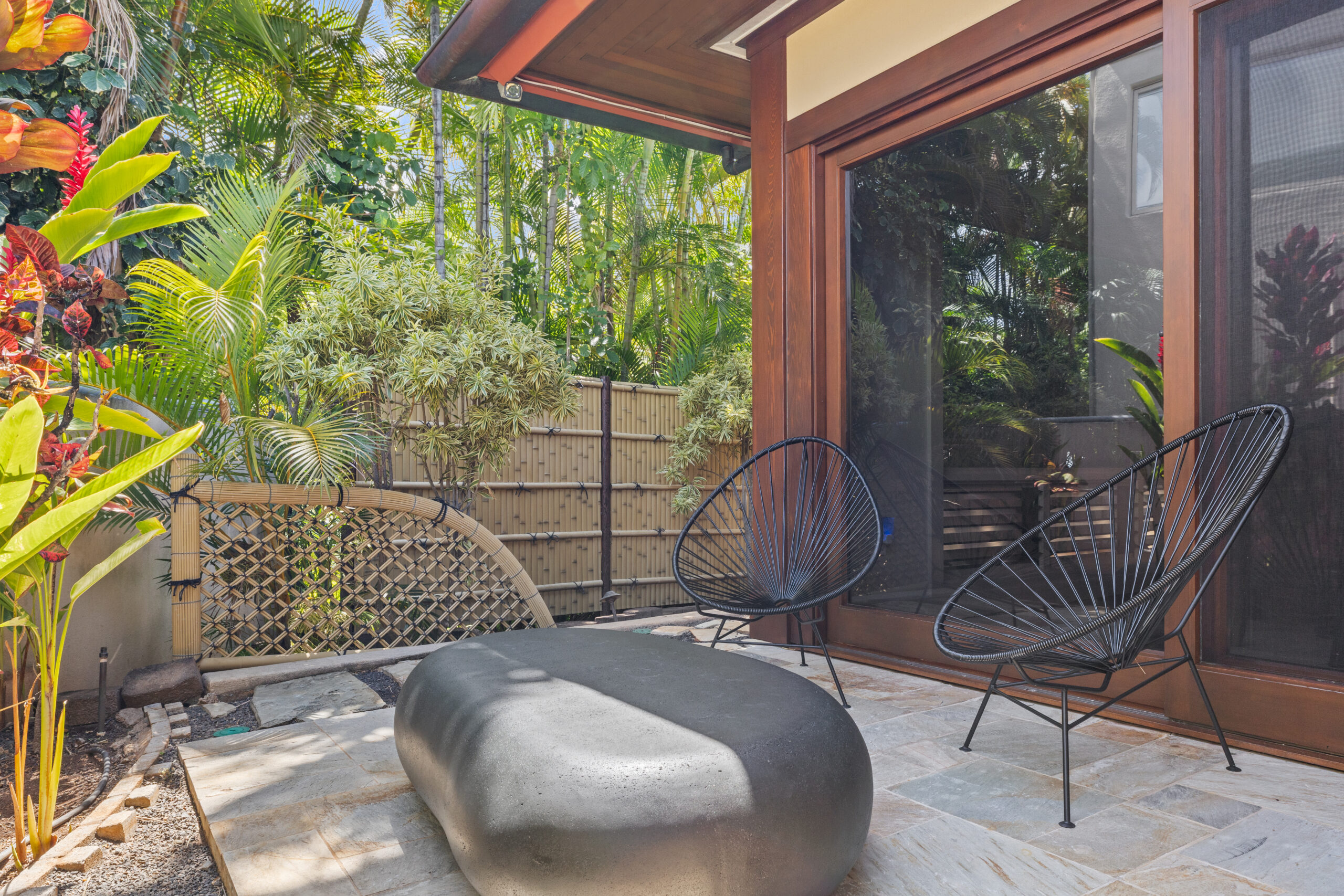 Private garden patio with two lounge chairs and a stone coffee table surrounded by tropical plants